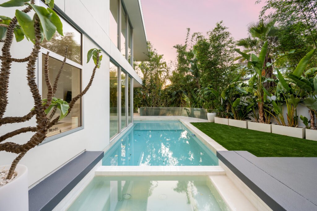 backyard pool with surrounding greenery and a tree